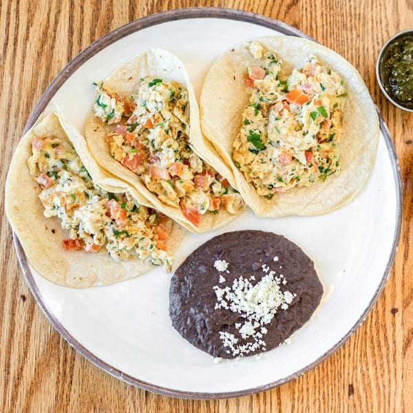 Three Polanquito breakfast tacos with scrambled eggs, pico de gallo, and a side of refried beans.