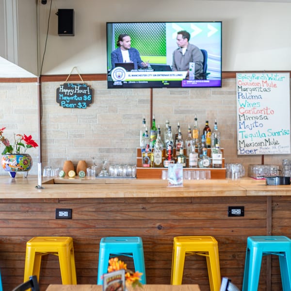 Polanquito's bar area with colorful stools, liquor bottles, a TV, and happy hour specials.