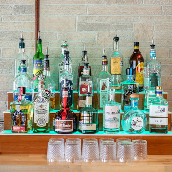 A bar shelf at Polanquito displays a wide selection of tequila and mezcal bottles, with glasses below.