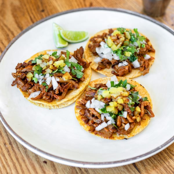 Three Polanquito tacos with meat, onions, cilantro, and pineapple, served with lime wedges.