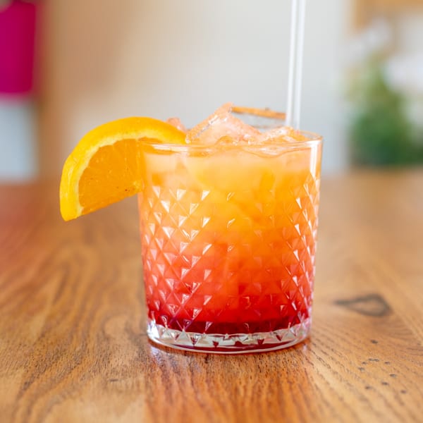 A vibrant, layered Polanquito Mexican cocktail with orange and red hues, garnished with an orange slice.