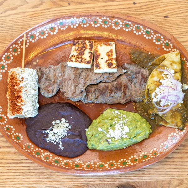 Polanquito's Mexican platter with grilled steak, elote, black beans, guacamole, and enchiladas on a decorative plate.