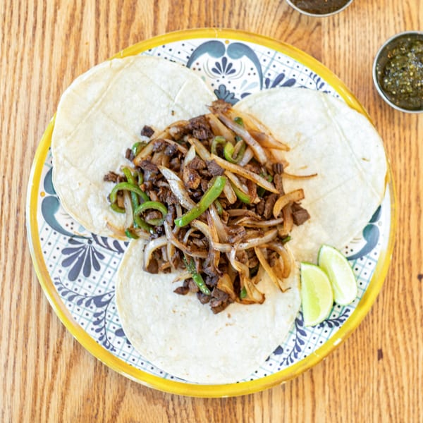Polanquito's carne asada tacos with grilled onions, peppers, and lime wedges on a decorative plate.