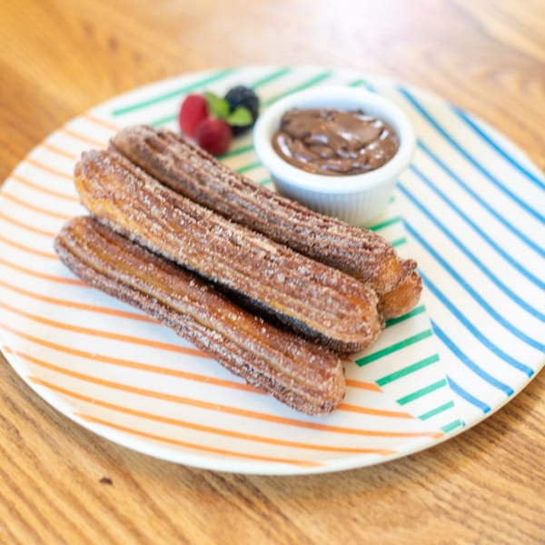 Polanquito churros with cinnamon sugar, chocolate dipping sauce, and fresh berries on a striped plate.