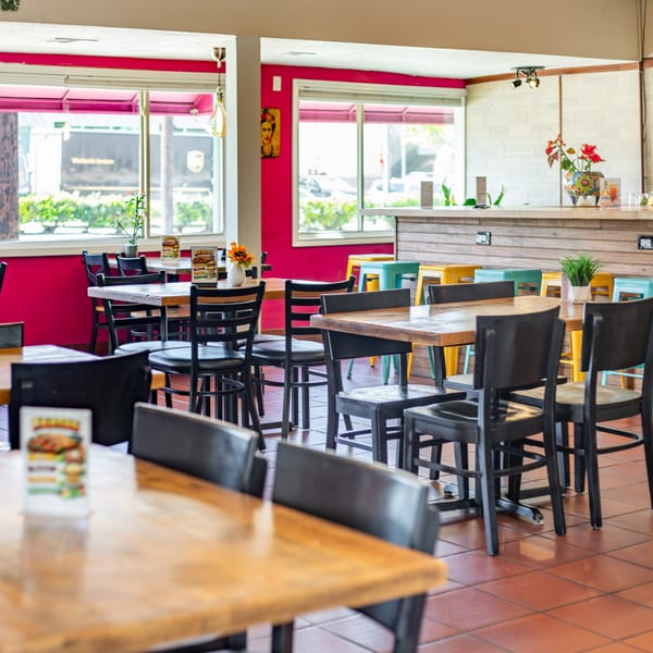 Polanquito's vibrant dining room with hot pink walls, wooden tables, black chairs, and a bar area.