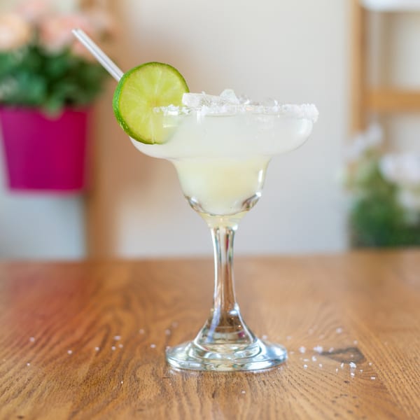 A Polanquito margarita with a salted rim, lime slice, and straw on a wooden table.