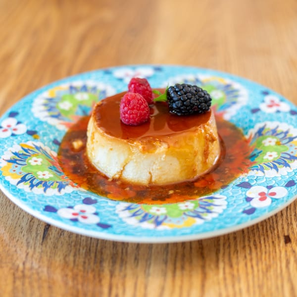 Polanquito's flan dessert with caramel sauce, raspberries, and a blackberry on a colorful plate.