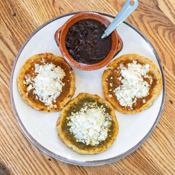 Three Polanquito sopes with green and red salsa, cheese, onions, and a side of black beans.