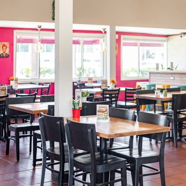 Brightly lit Polanquito dining room with wooden tables, black chairs, and vibrant pink walls.