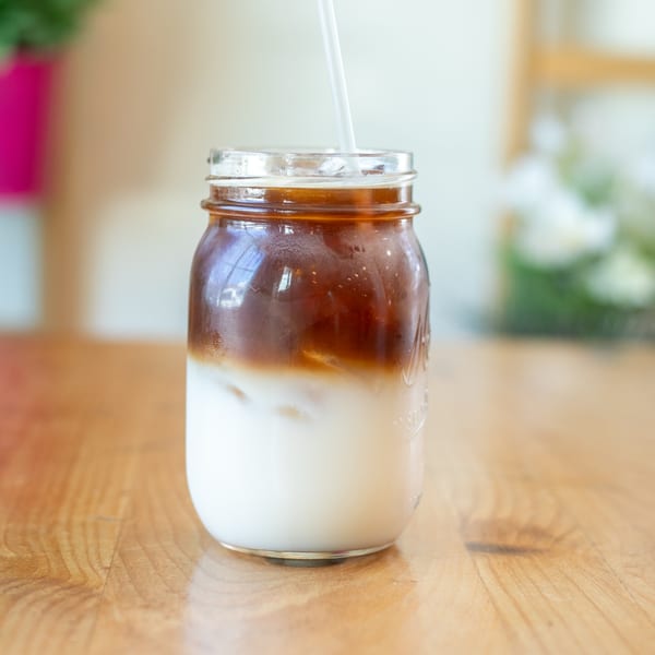 Iced coffee with milk in a mason jar with a straw on a wooden table.