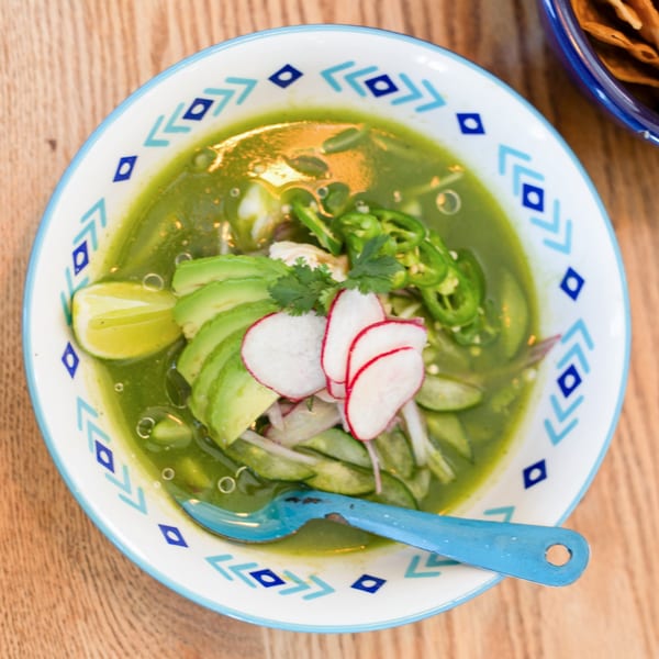 Polanquito's green pozole with avocado, radishes, lime, and serrano peppers in a patterned bowl.