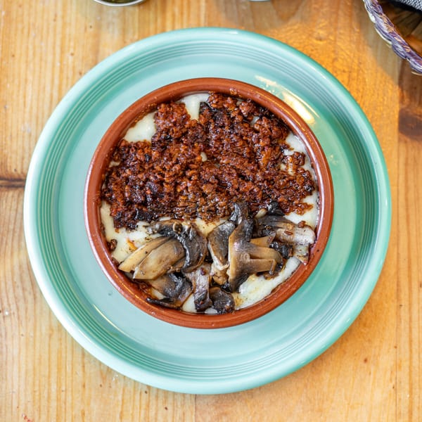 Polanquito's melted cheese dish with chorizo and mushrooms, served in a brown bowl on a teal plate.