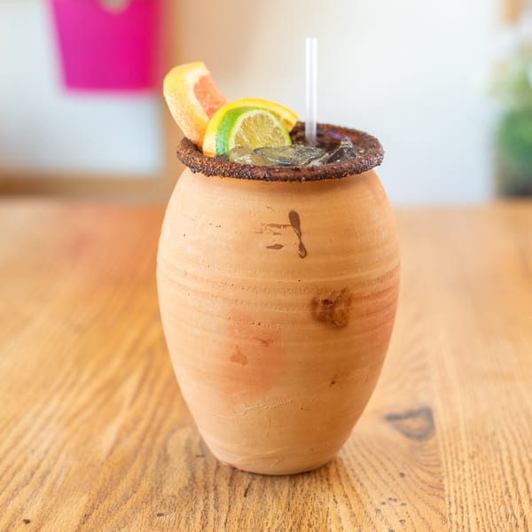 A Mexican cantarito cocktail in a clay pot, garnished with grapefruit and lime slices.