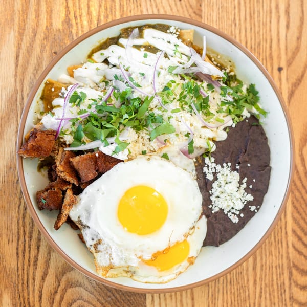 Polanquito's chilaquiles with green salsa, fried eggs, beans, and carnitas on a wooden table.