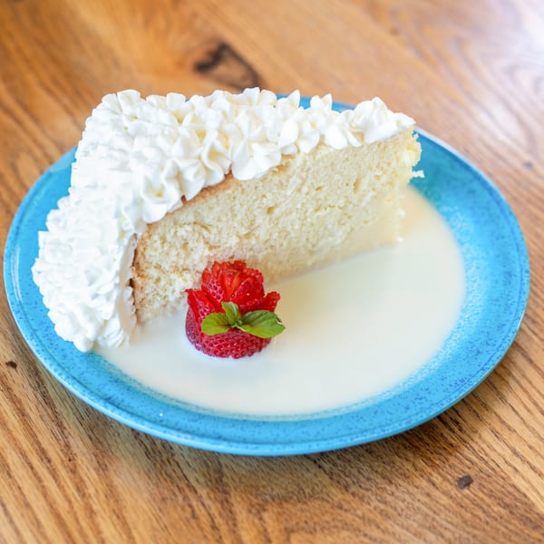 A slice of tres leches cake with whipped cream, a strawberry rose, and mint on a blue plate.